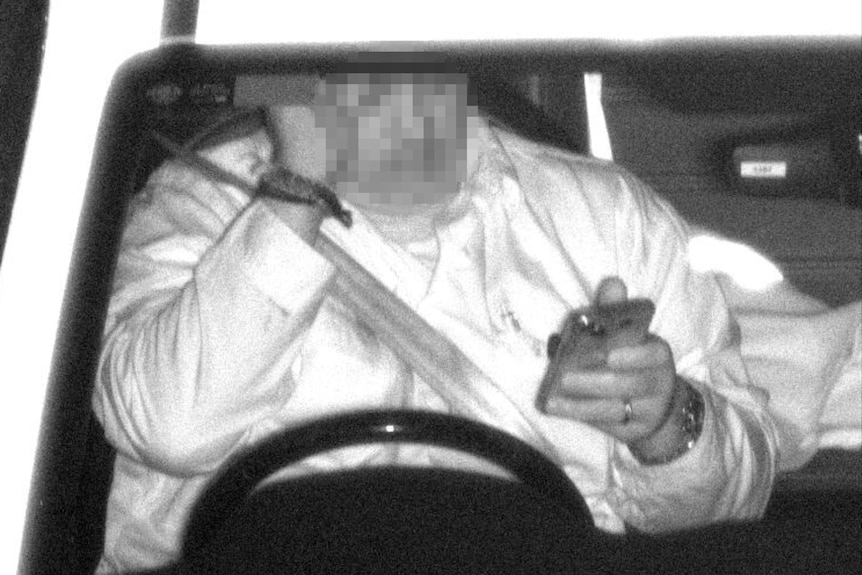 A zoomed-in speeding camera image of a person in the driver's seat holding a mobile phone.