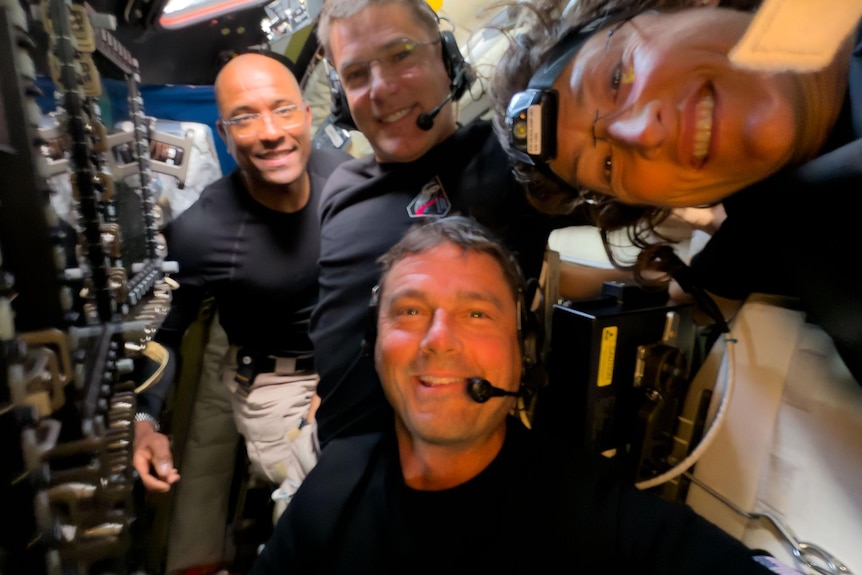 four astronauts smile at the camera inside their spacecraft 