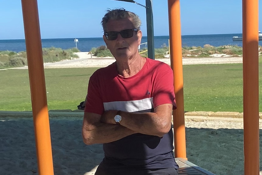 A man wearing sunglasses stands next to equipment at a children's playground.