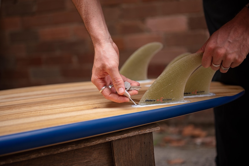 Surfboard fins being put onto a surfboard.