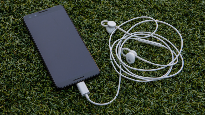 A Google Pixel phone on the grass with a pair of wired earbuds connected to it.