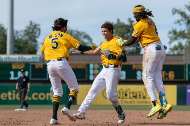 The Athletics' Jacob Wilson, left, and Lawrence Butler, right, celebrate with Max Muncy after he hit a walk-off sacrifice fly during the 11th inning against the White Sox on Saturday, April 18, 2026, in West Sacramento, Calif. (AP Photo/Sara Nevis)