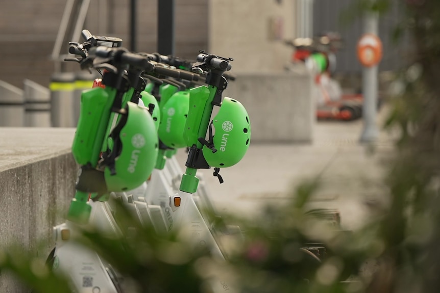 Five green Lime scooters are parked in a line by a concrete block