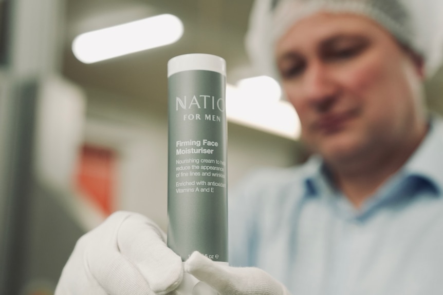 Aleks is blurred, he holds a green Natio for men firming face moisturiser tube for in hand.