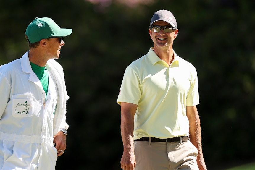 Adam Scott and his caddy smile as they walk the Masters course.