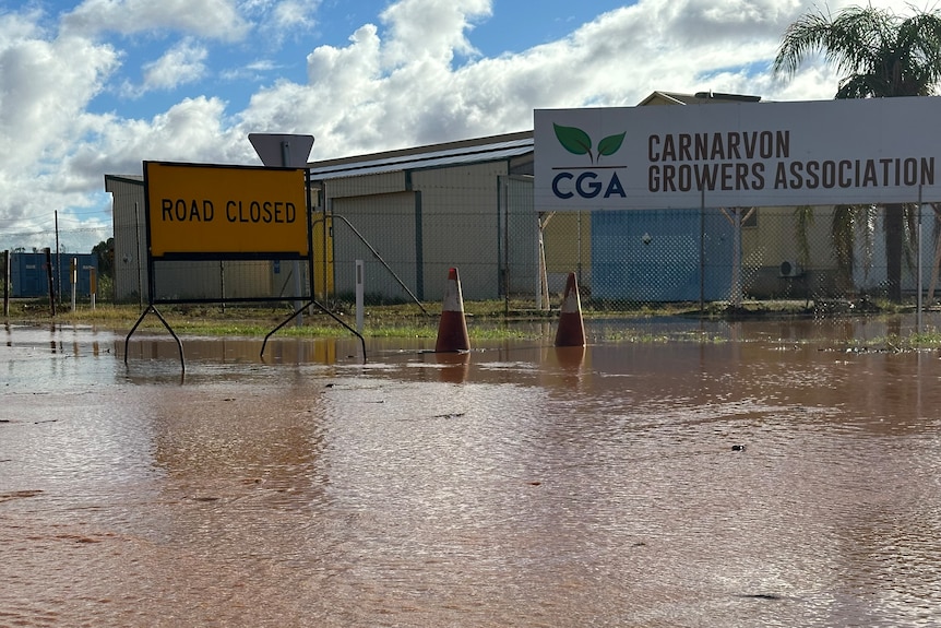 A sign that says "road closed" sits outside the fence of a flooded business.