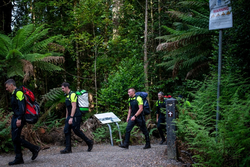 Four police officers in black and yellow hi-vis walking out of a forest