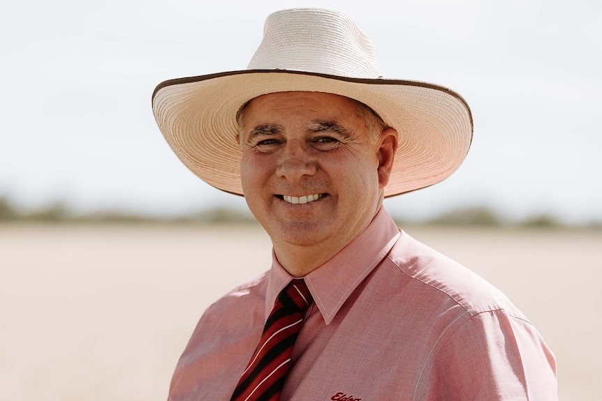 A head-and-shoulders picture of a smiling man n a wide hat and striped tie.