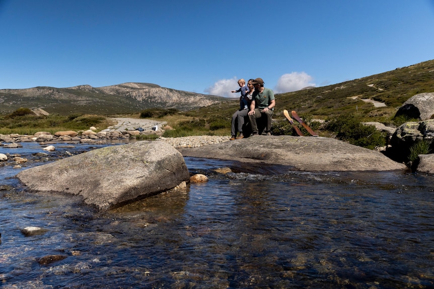 A family sitting near a stream in a green mountain.