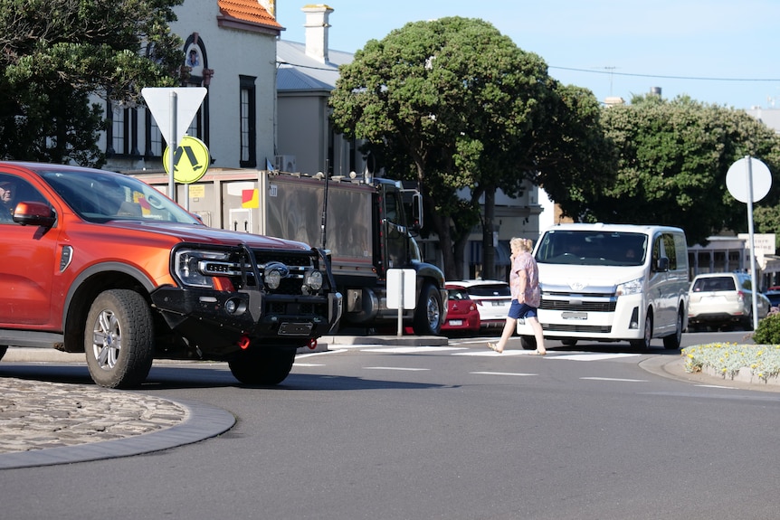A pedestrian walking across a crossing in Warrnambool with cars nearby.