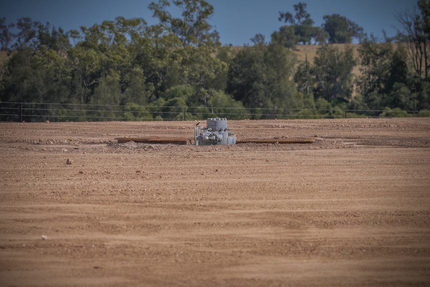 A pipe pokes up through a hole in a dusty field.