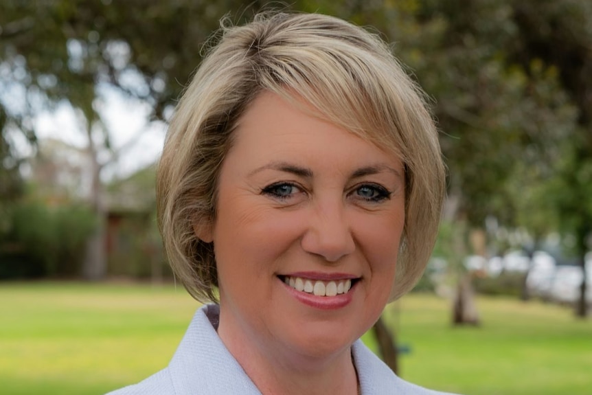 A woman with short blonde hair wearing a white jacket