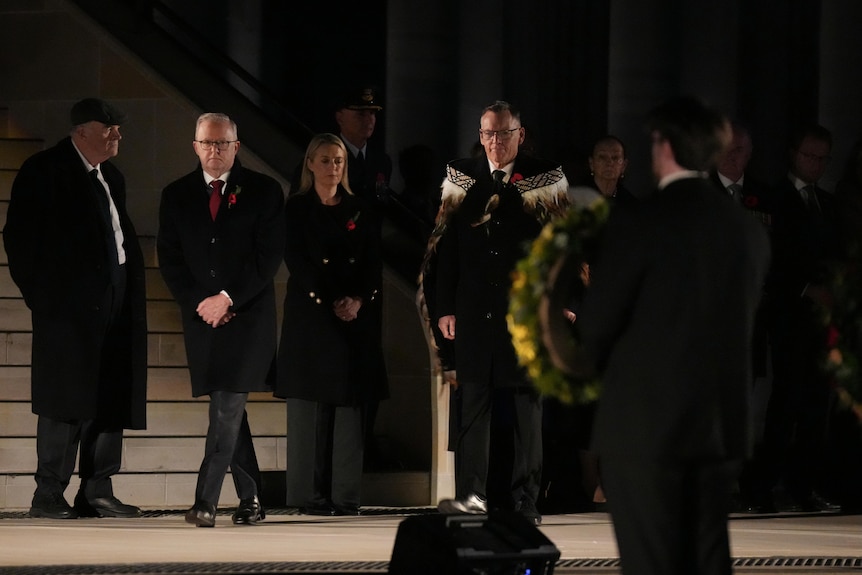 A group of people wearing dark clothes stand in the darkness at the ceremony.