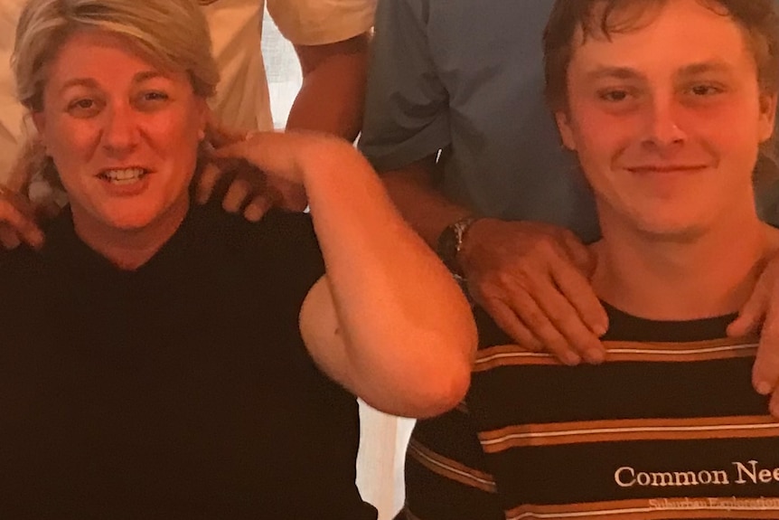 Blonde woman smiling next to brunette son in stripped shirt.