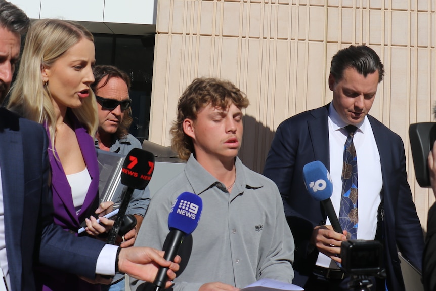 Brodie Dewar leaves court surrounded by reporters holding microphones. 