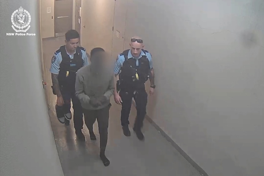 Michael Angok in handcuffs being walked into blacktown police station by two officers