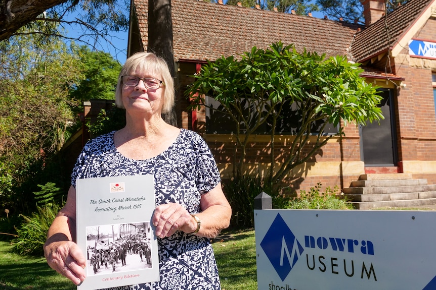 A woman holds a book in front of a historic building.