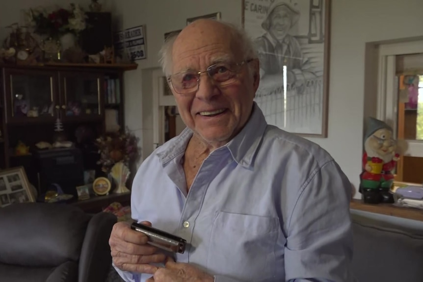 Elderly gentleman smiling while holding harmonica in lounge room.