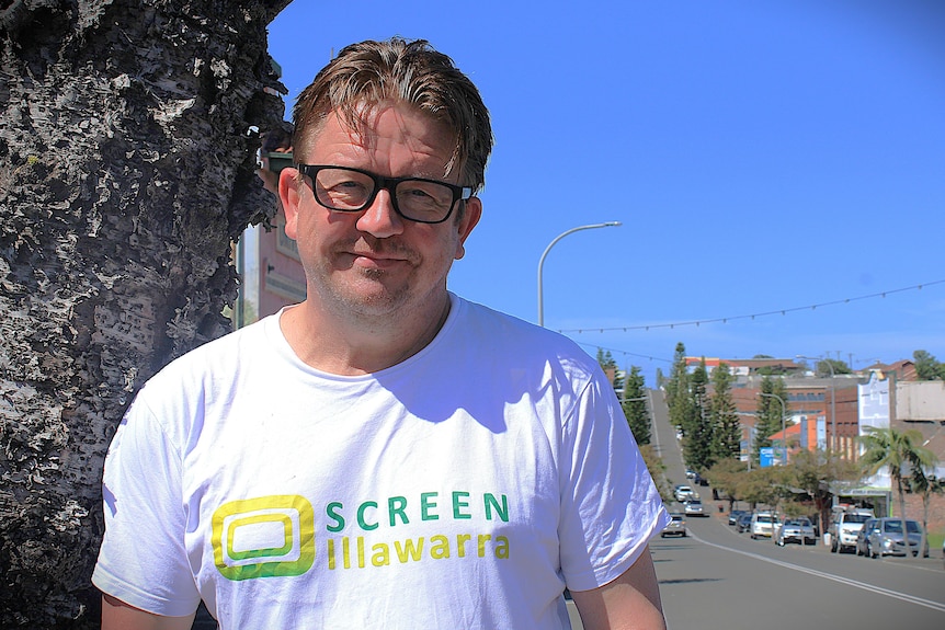 Man with brunette hair and glasses, white shirt, smiling in Port Kembla main street