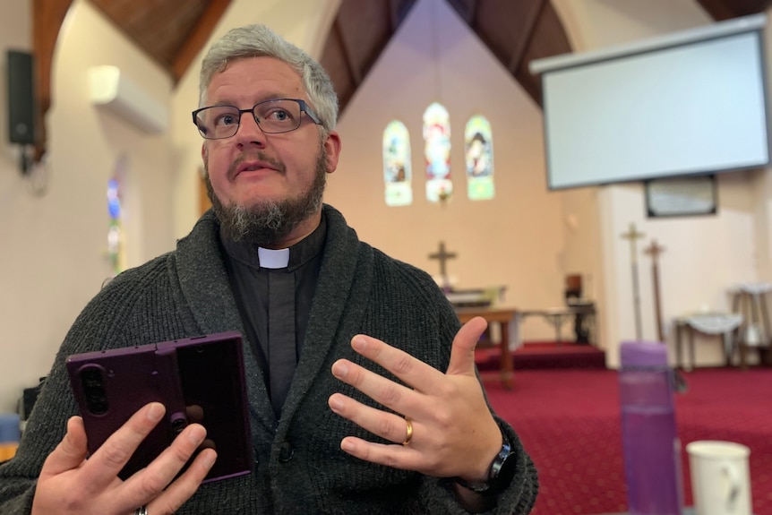 David Perryman in his clerical clothing in a church, holding a bible.