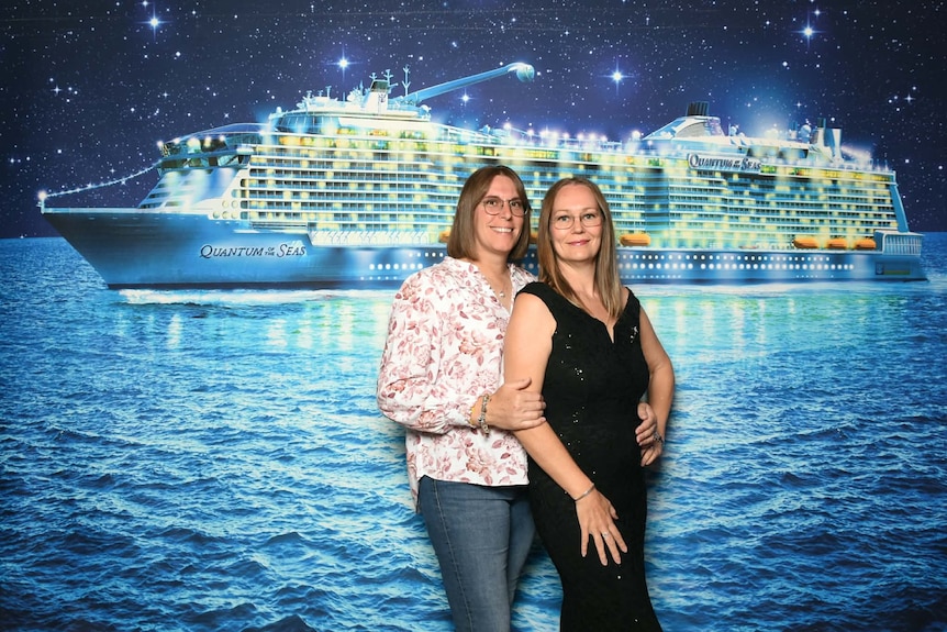 Two women posing for a photo in front of a large banner of a cruise ship