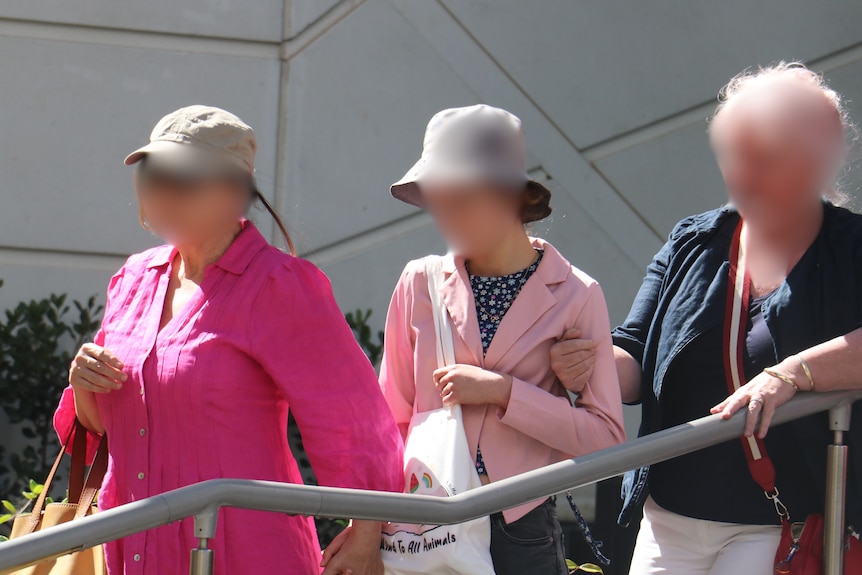 Three women with blurred faces walk down stairs outside a court. One is young and two are older.