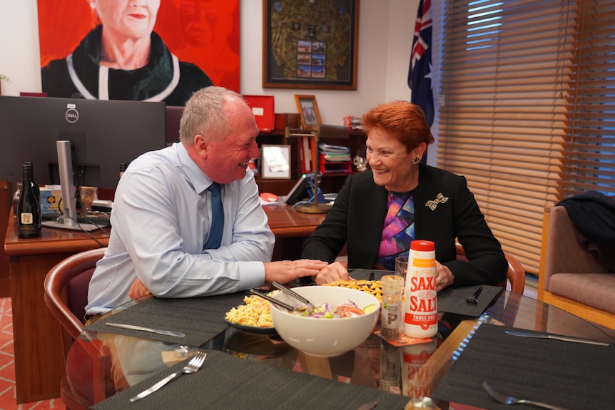 A man and a woman eating dinner together in an office and laughing.