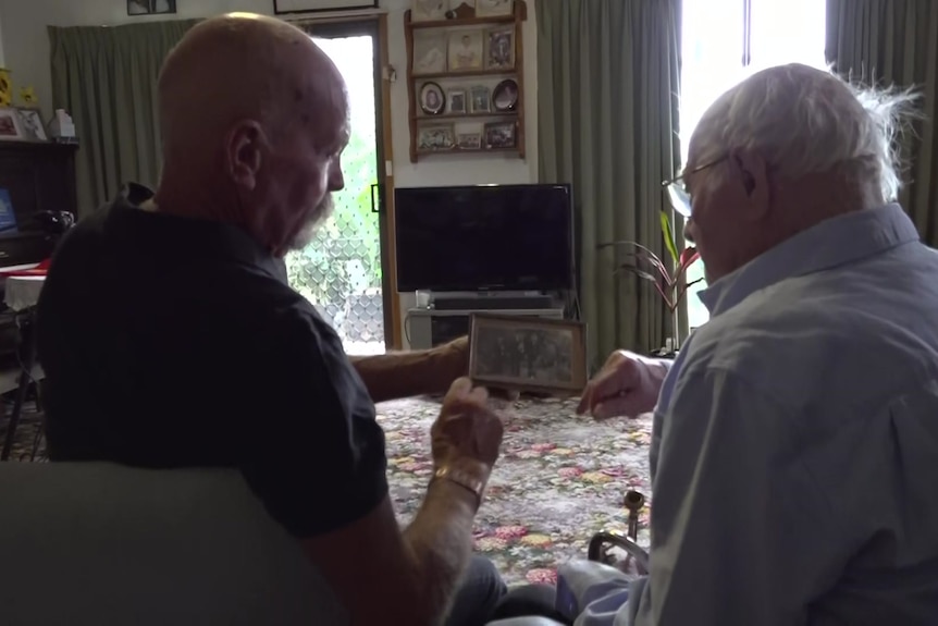 Middle aged man and elderly gentleman looking at a framed photo together in a lounge room