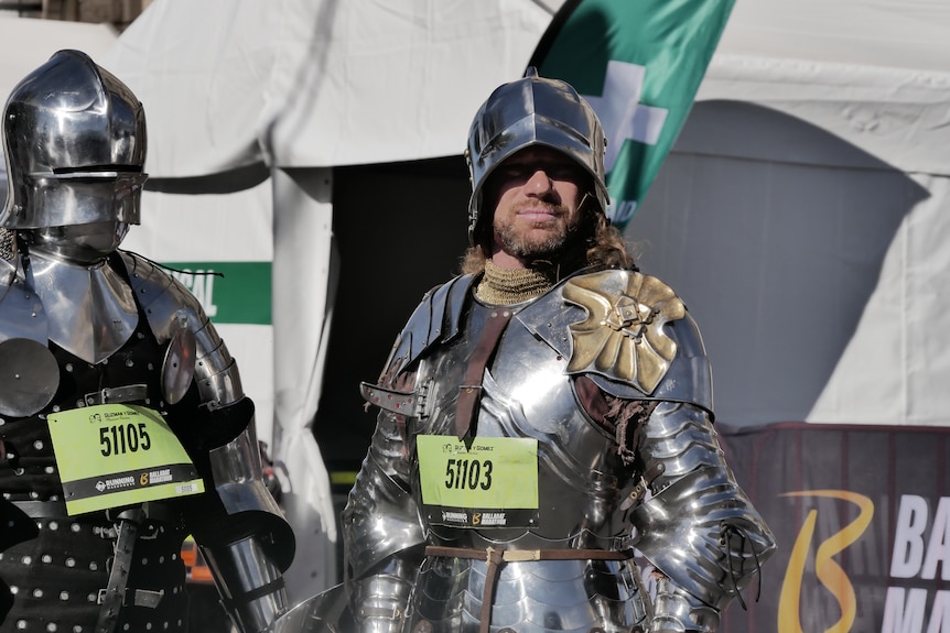 A man in a full suit of armour looks at the camera