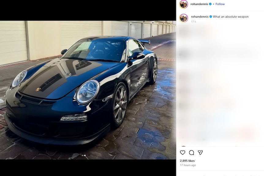 A black porsche in a driveway next to a row of garages, the floor is wet