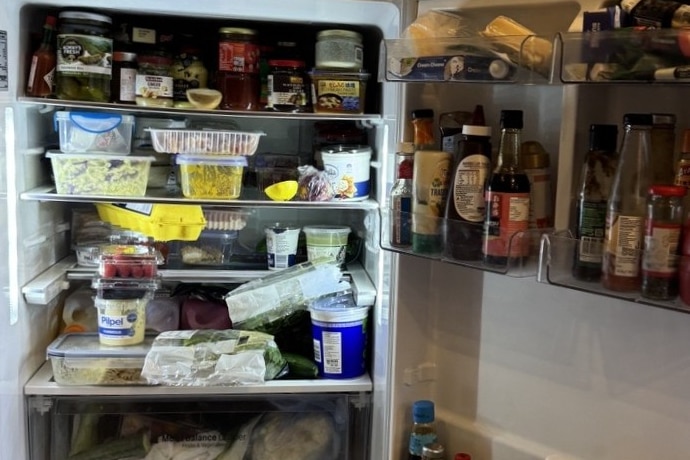 A very crowded share house fridge, featuring a lot of condiments. 