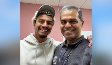 Young man in a baseball cap with his arm around another man both smiling