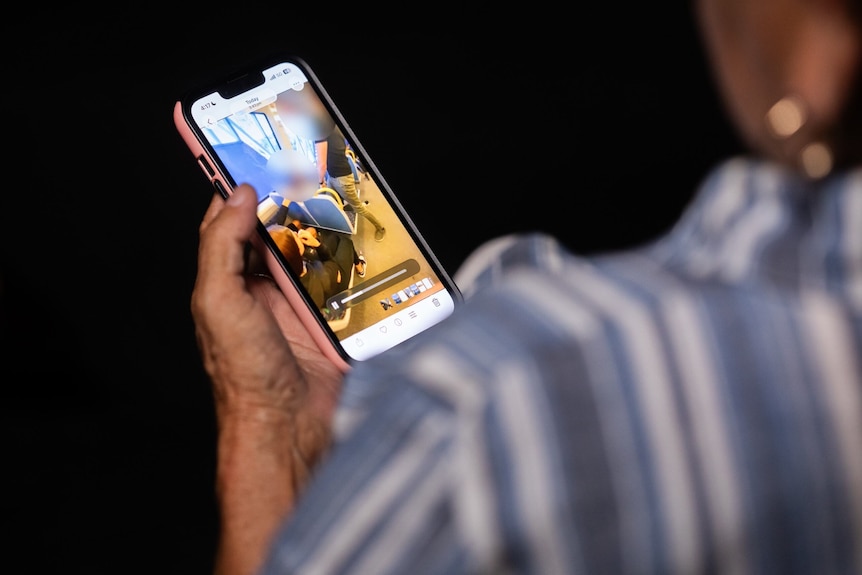 A woman in a striped shirt watches a video on a mobile phone 