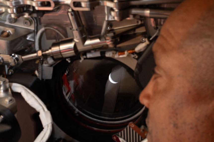 A man peers through a spacecraft's porthole, through which the Earth is visible.