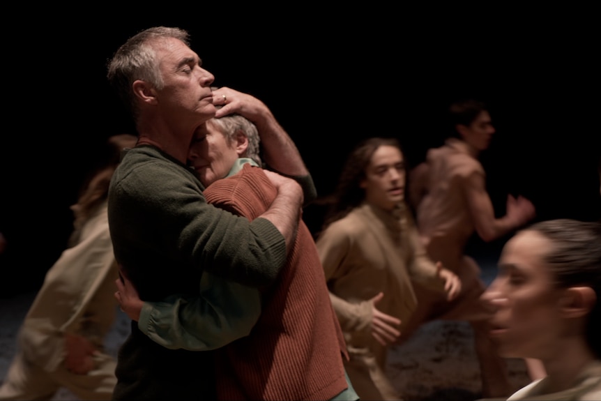 Greg Wise and Emma Thompson embrace like they never want to let each other go. Dancers rush around them in the background.