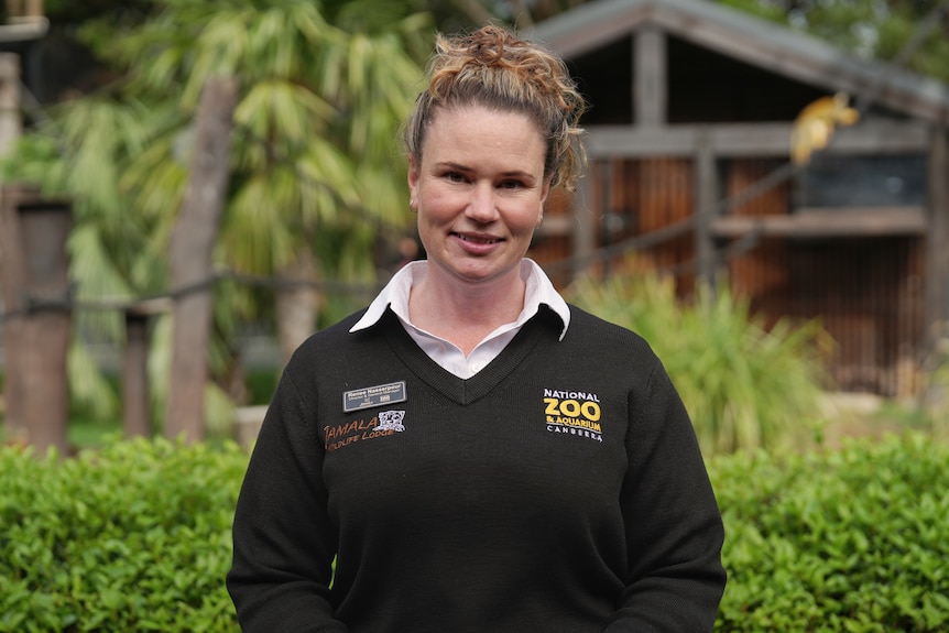 A woman in a National Zoo jumper stands in front of an enclosure.
