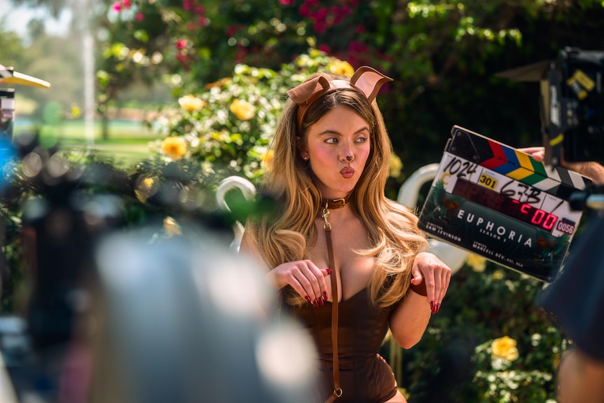 A woman dressed as a sexy dog stands outside behind a camera and a clapboard