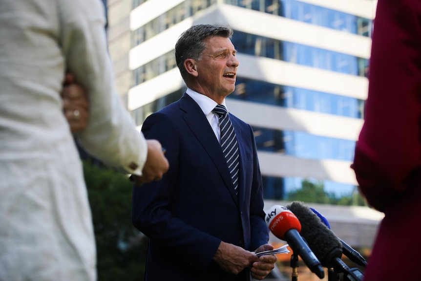 A mid-shot of Federal Opposition Leader Angus Taylor speaking into microphones during a doorstop outside, in a suit and tie.