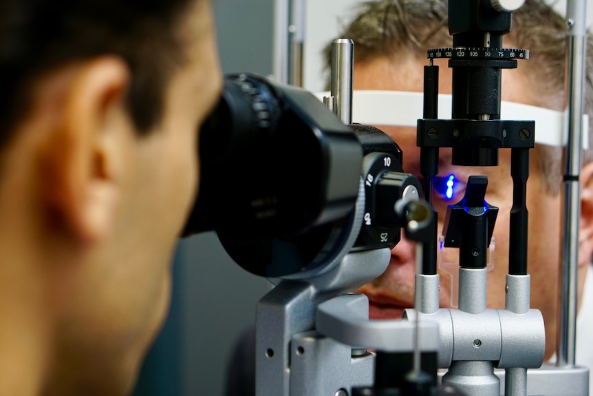 A man uses equipment to analyse someone's eyes with a blue light.