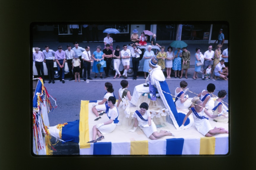 A group of women dressed as royalty sit around a float with a queen sitting on a throne above them during a festival.