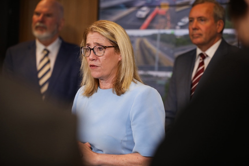 Rita Saffioti stands in a Main Roads operations centre speaking at a media conference, with two men and CCTV screens behind her.
