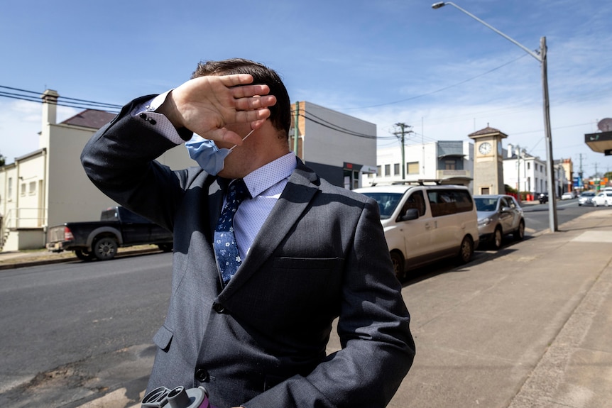 A man in a suit walking along with his hand covering his face.