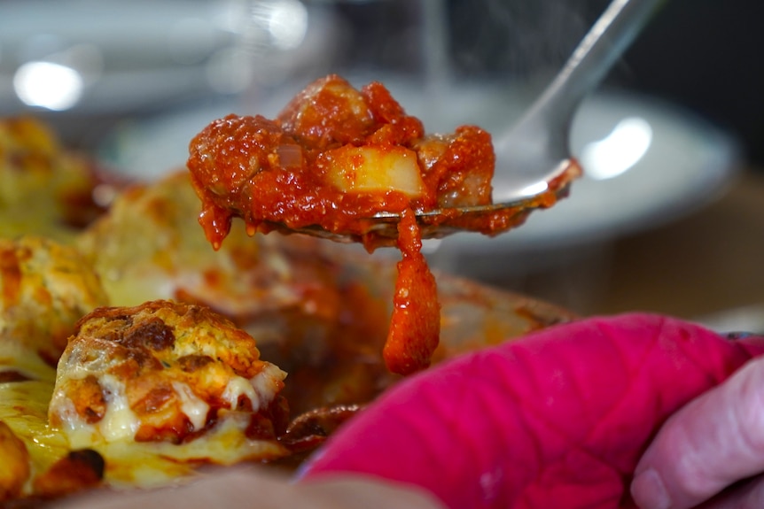 A spoon filled with sauce-covered cooked vegetables coming out of a baking tray