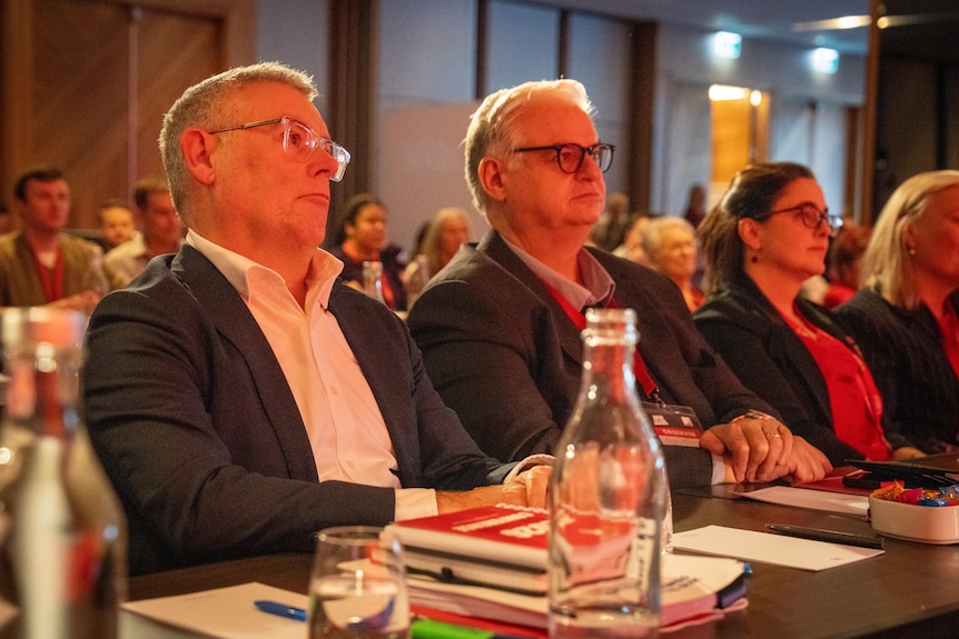 Two middle aged male politicians, and a female politician, sit attentively.