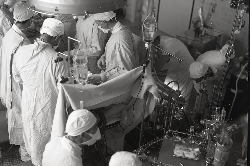 A black and white photo of a team of surgeons operating on a heart.