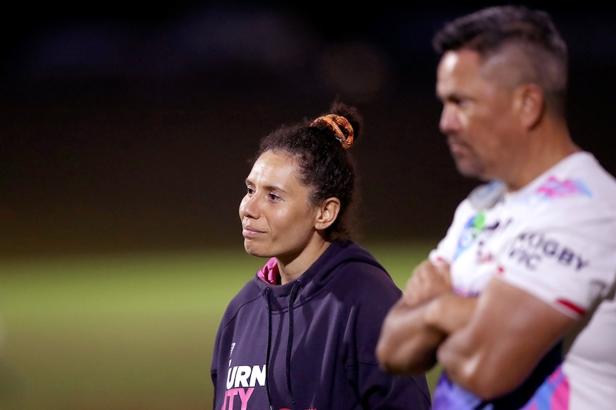 Melanie Kawa, dressed in a hoodie, looks on seriously during a night time Super W training session.