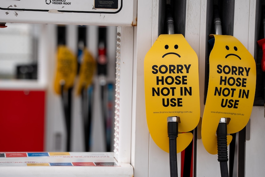 Two fuel nozzles with signs saying :( SORRY HOSE NOT IN USE