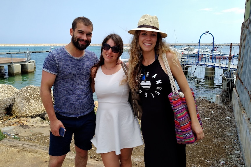 Two women and a man pose on a shore.