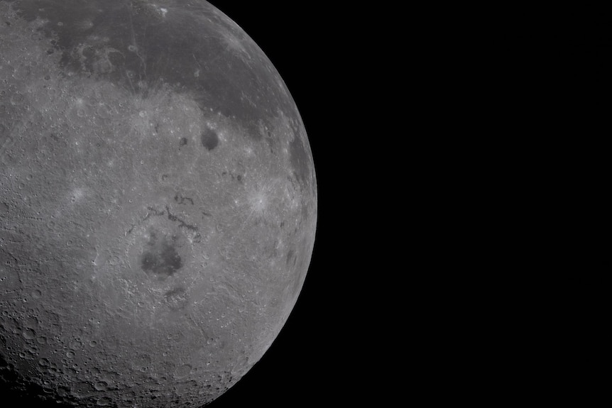 Half of the Moon fills the left half of the image. The near side, characterized by the dark patches of ancient lava