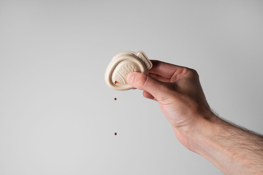 A person's hand squeezing drops of soy sauce from a beige-coloured biodegradable fish-shaped container.